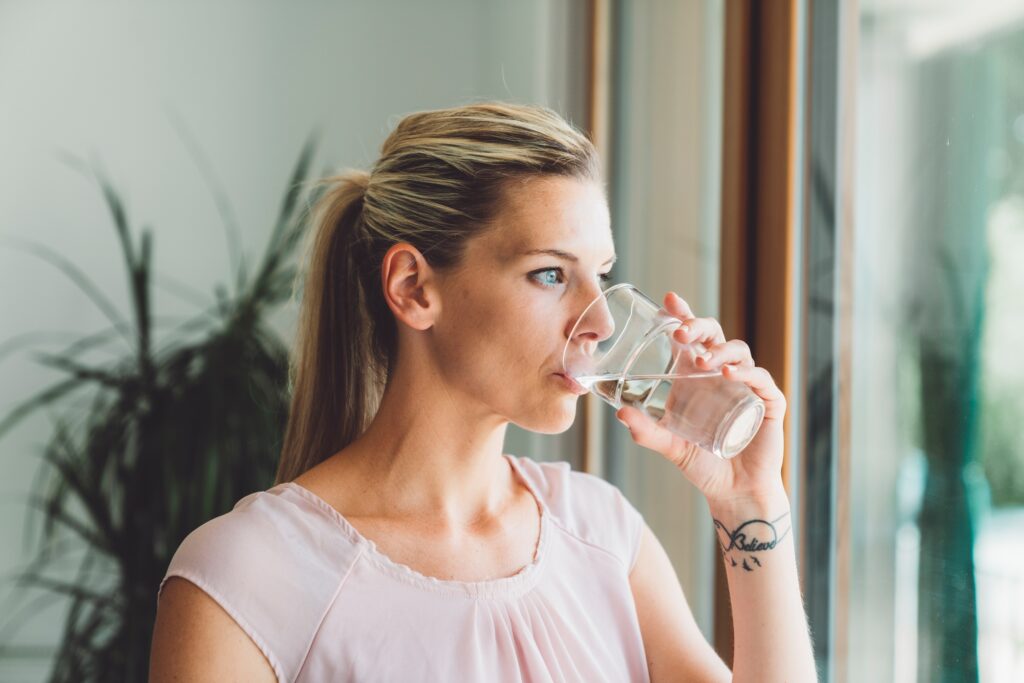 Waist up portrait of caucasian woman drinking a glass of water while looking out the window