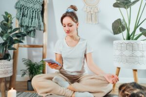Young healthy woman using phone for setting mobile app for meditation at home,