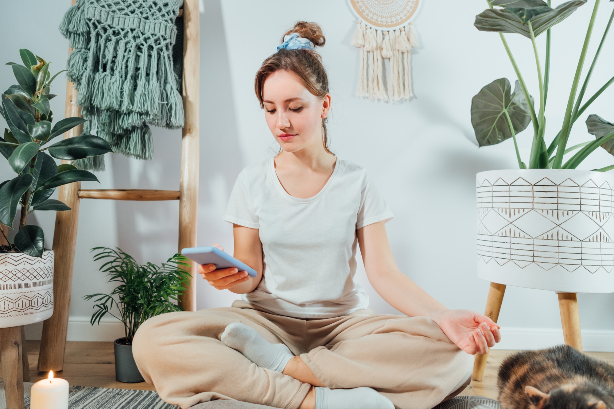 Young healthy woman using phone for setting mobile app for meditation at home,